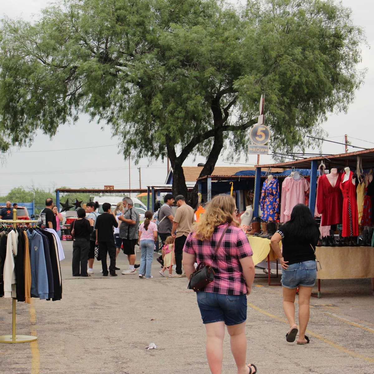 Shoppers browsing racks of clothing at an outdoor flea market, taken by Joshua Gest